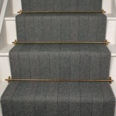 a carpeted stair case with gold hardware on the top and bottom steps in grey herringbone