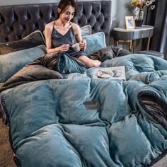 a woman sitting on top of a bed next to a blue comforter and pillows