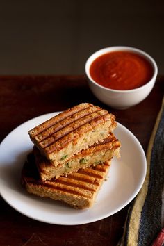 two grilled sandwiches sit on a plate next to a bowl of tomato soup and a napkin