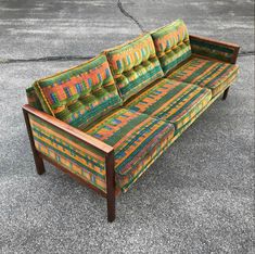 a colorful couch sitting on top of a cement floor next to a wooden frame and foot rest