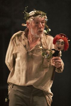 an old man holding a doll with flowers in his hair and wearing a red headdress