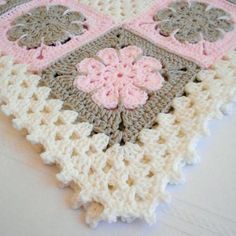 a crocheted blanket with pink and gray flowers on the bottom is laying on a white surface