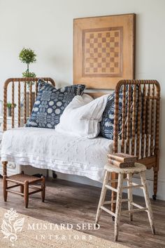 a white bed with blue and white pillows in a room next to a wooden chair