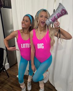 two women dressed in pink and blue posing for the camera with one holding a blow dryer