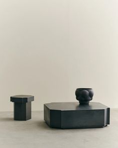 two black vases sitting on top of each other in front of a white wall