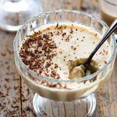 a dessert in a glass bowl on a wooden table with two glasses and spoons