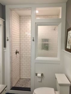 a white toilet sitting under a window next to a walk in shower and bathtub