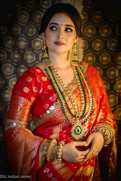 a woman in a red and gold sari with green beads on her necklaces