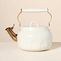 a white tea pot with a gold handle and a curved handle on the top, sitting on a table