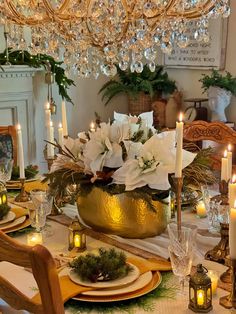 a dining room table set for christmas with candles and flowers in a gold bowl on it