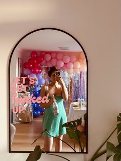 a woman taking a selfie in front of a mirror with balloons and streamers