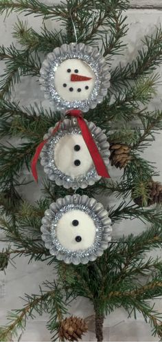 three snowman ornaments hanging from a pine tree