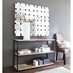 a mirror and some books on a shelf in front of a wall with a vase