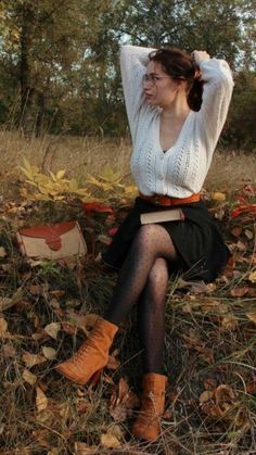 a woman sitting on top of a pile of leaves in the grass with her hands behind her head