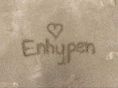 the word enhypen written in sand with a heart on it's side