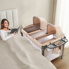 a woman sitting on a bed reading a book next to a baby crib and changing table