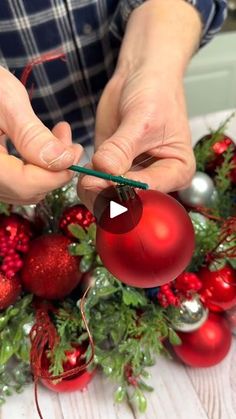 a person is decorating christmas balls and greenery