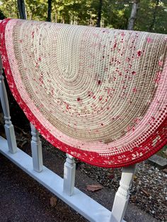 a red and white crocheted blanket sitting on top of a wooden rail next to trees