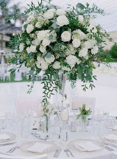 a vase filled with white flowers sitting on top of a table covered in plates and glasses