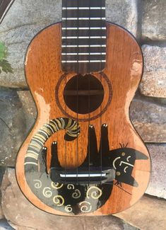 a wooden guitar with an animal on it's back and neck, hanging from a stone wall