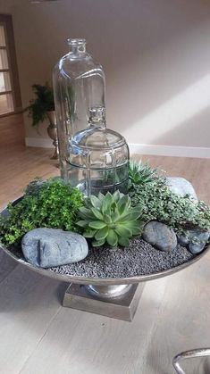 there is a glass bottle and some plants on a tray with rocks in the middle