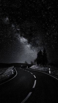 the night sky is filled with stars above a road and some trees in the distance