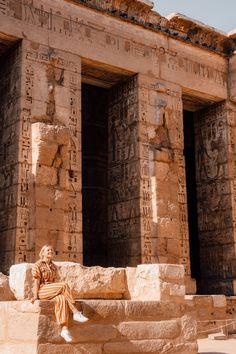 a woman sitting on some steps in front of an ancient building with columns and carvings