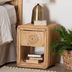 a wicker side table with books and a lamp on it next to a bed