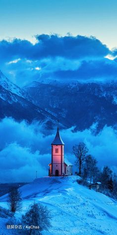 a church on top of a snow covered hill with mountains in the background at dusk