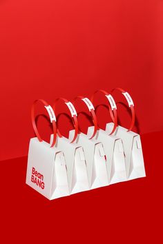 four white paper bags with red handles are lined up against a red background and each bag has a ring on it