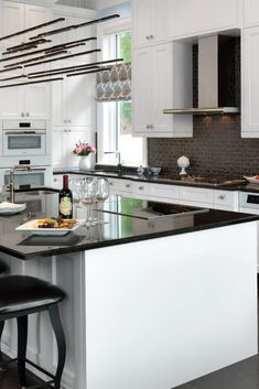 a kitchen with white cabinets and black counter tops, an island in the middle has wine glasses on it