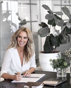 a woman sitting at a table with a pen and paper in front of her smiling