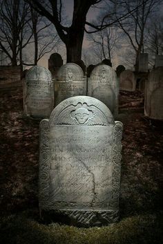 an old cemetery with headstones and trees in the background at night, lit up by street lights