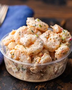 a glass bowl filled with shrimp salad on top of a wooden table next to a fork