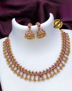 This beautiful temple jewelry set is crafted with exclusive South Indian style matte gold and embellished with ruby and emerald stones. The simple choker necklace is paired with Jhumka earrings for a stunning look, perfect for gifting to a loved one. Gold Necklace Stone Jewelry, Ruby Jewelry Necklaces Indian, Ruby Emerald Necklace Indian, Stone Necklace Gold Indian, South Indian Jewellery Necklace Set, Unique Gold Necklace Designs, South Indian Gold Jewellery, Ruby Necklace Indian