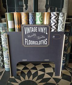 an assortment of floorcloths are on display in a store window, with the sign for vintage vinyl