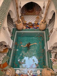 a woman swimming in a pool surrounded by tiled walls and pillars with columns on either side