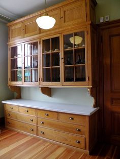 an empty kitchen with wooden cabinets and white counter tops on hard wood floors in front of a window