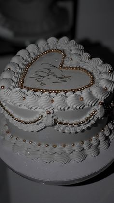 a wedding cake with white frosting and gold beads on it's edges, decorated with a heart