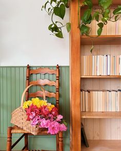 a wooden chair sitting next to a bookshelf filled with lots of books and flowers