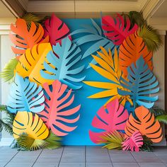 colorful paper cut out leaves on a blue wall in front of palm trees and houseplants