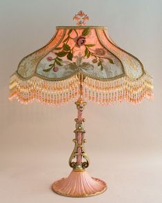 a pink lamp that is on top of a white table with beaded lampshade