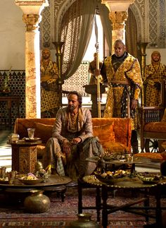 two men sitting on couches in a living room with gold and white decorations around them