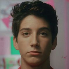 a close up of a person wearing a red shirt and looking at the camera with a serious look on his face