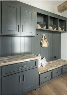 a kitchen with green cabinets and wooden counter tops, baskets on the wall above it