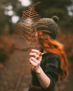 a woman with red hair is holding a fern