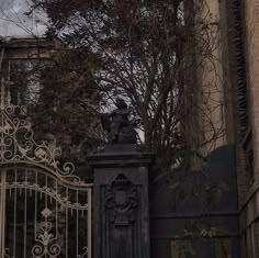 an iron gate with a statue on top in front of a brick building and tree