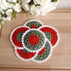 three crocheted coasters sitting on top of a wooden table next to white flowers