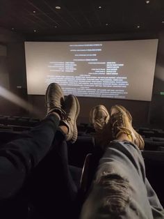 two people sitting in front of a screen with their feet propped up on the ground