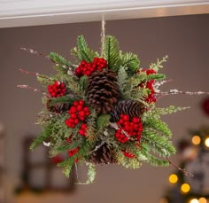 a christmas decoration hanging from a ceiling with pine cones and berries on the top, surrounded by greenery